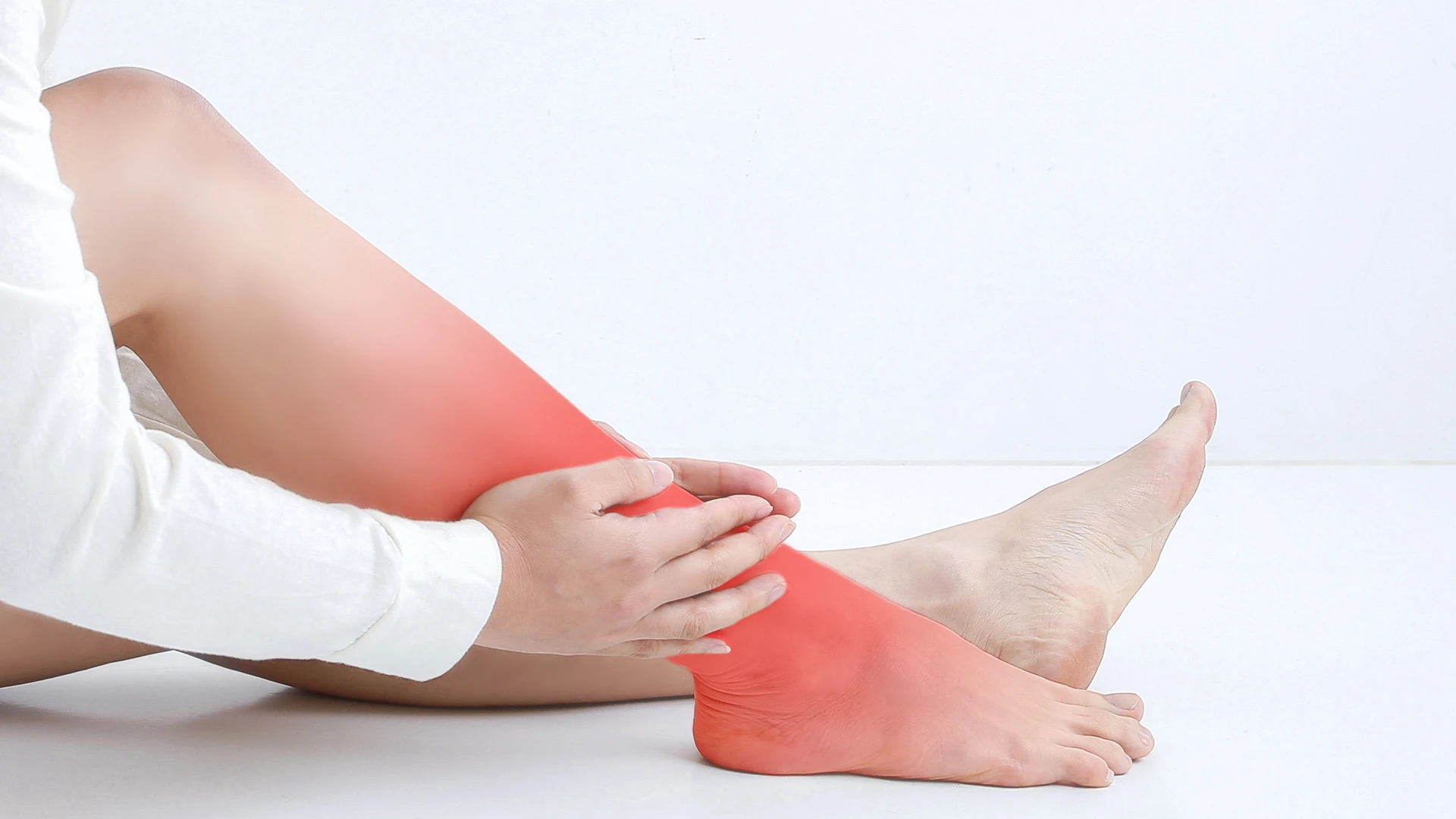 Ból, zaczerwienienie i obrzęk nogi - objaw zakrzepowego zapalenia żył. Pacjent trzymający obolałą łydkę na białym tle. Czerwone zaznaczenie wskazuje miejsce bólu i stanu zapalnego w nodze. Obrazuje typowe symptomy chorób żylnych wymagających konsultacji flebologa.