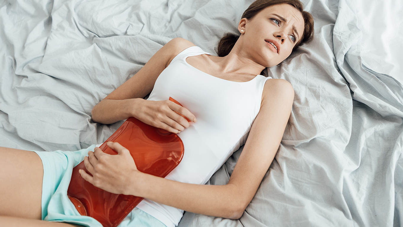 Młoda kobieta trzymająca termofor cierpiąca na obfite miesiączki i anemię.